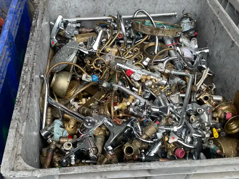 Achat de fer et de métaux en essonne Une grande poubelle remplie de divers accessoires de plomberie, tuyaux, valves et robinets en métal mis au rebut - certains avec des tuyaux attachés - dans un centre de recyclage ou de ferraille spécialisé dans l'achat de fer et de métaux en Essonne.